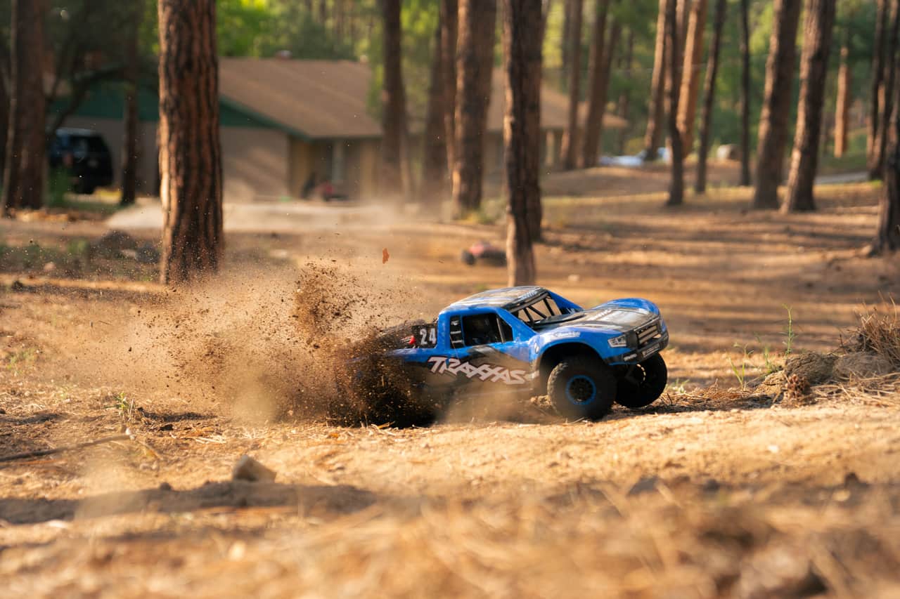 A four-wheel-drive radio-controlled truck throwing up dirt on a wooded trail